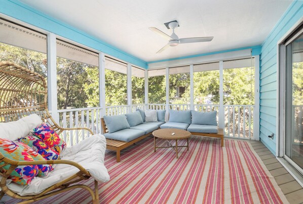 A covered porch with a ceiling fan, a wicker chair, a sofa with cushions, and a striped rug.