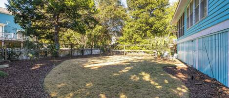 A backyard with a grassy area, trees, a fence, and a blue building.