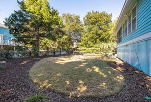 A backyard with a grassy area, trees, a fence, and a blue building.