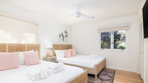 Hotellihuone, jossa on kaksi sänkyä, kattotuuletin, ikkuna, josta on näkymä puita kohti, ja kudottu matto.