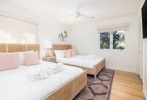 A hotel room with two beds, a ceiling fan, a window with a view of trees, and a woven rug.