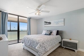 A bedroom with a bed, a nightstand, a ceiling fan, a view of the ocean, and a motivational quote on the wall. - Sweeping Ocean Views - Shores of Madeira #504 (Madeira Beach)
