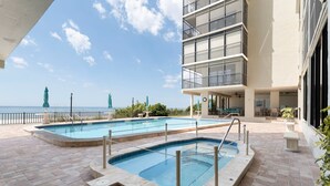 A pool area with two pools, a balcony, and a view of the ocean.