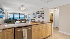 A modern kitchen with a large island, a dining area with a view, and a ceiling fan.