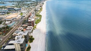 An aerial view of a coastal city with a long beach, modern buildings, and a clear blue sea.