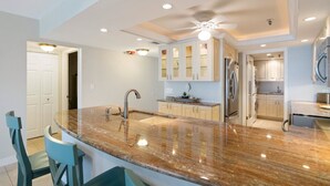 A modern kitchen with a curved granite countertop, stainless steel appliances, and a ceiling fan.