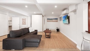 A spacious living room with a dark grey sectional sofa, a small wooden coffee table, and a TV mounted on the wall. - Beautiful ground floor unit in Central Point Lookout (Point Lookout)