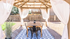 A covered patio with a wooden table and chairs, a patterned rug, and a potted plant.