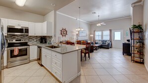 Une cuisine moderne avec des meubles blancs, un grand îlot central, des appareils en acier inoxydable et un coin repas comprenant une table et des chaises.