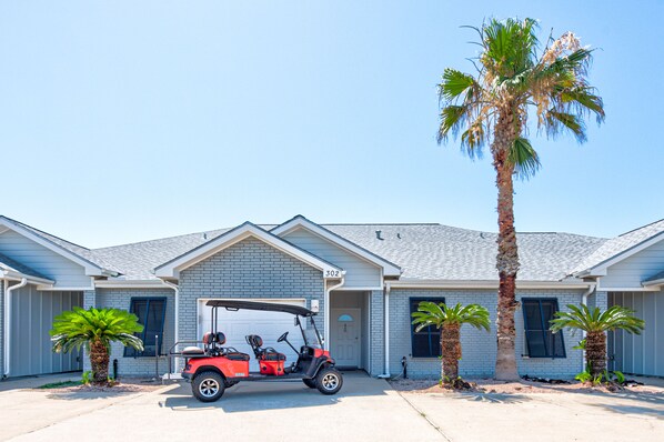 Un immeuble résidentiel avec un garage, une voiturette de golf rouge et des palmiers.
