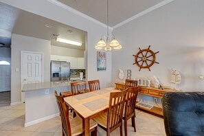 Un coin repas avec une table et des chaises en bois, une cuisine en arrière-plan et une décoration sur le thème de la marine.