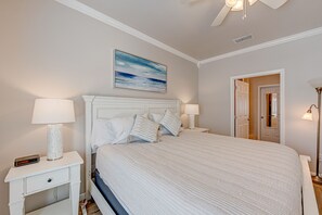 Une chambre à coucher comprenant un lit, deux tables de chevet, une commode, un ventilateur de plafond, un tableau et une porte.