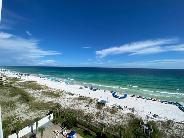 A beach with white sand, clear blue water, and a few umbrellas.