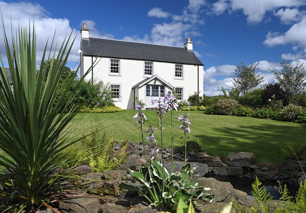 A white house with a grey roof, surrounded by a well-maintained lawn and flowering plants. - Luxury Scottish farmhouse (Perth)