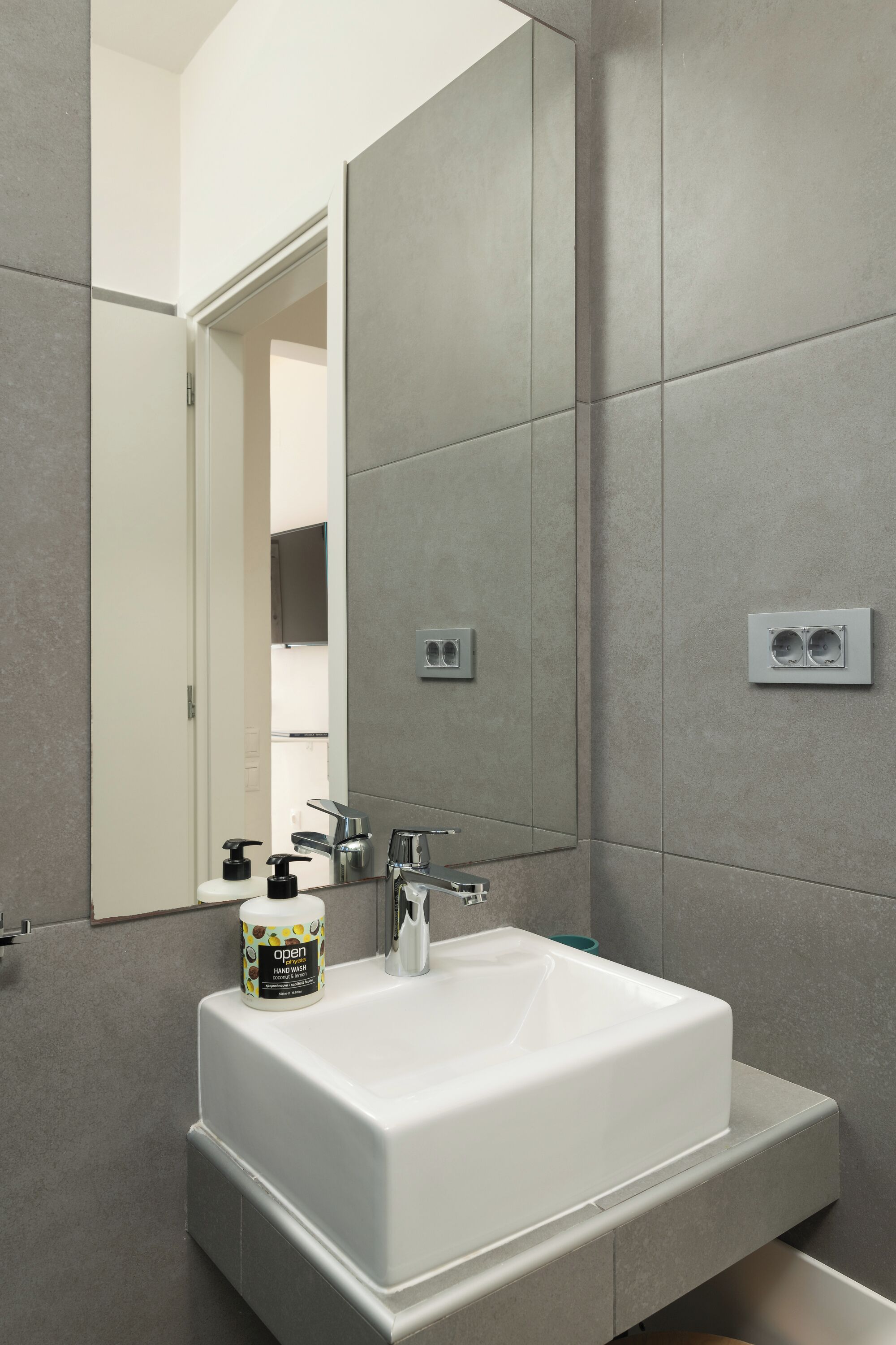 Une salle de bain moderne avec un lavabo blanc, un miroir et un porte-rouleau de papier toilette.