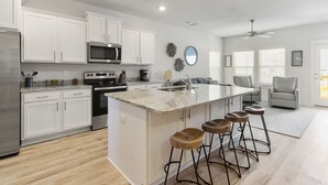 A modern kitchen with white cabinets, a granite countertop, and a central island with stools. - Bring The Whole Family And Friends, Too! White Beaches Are Waiting! (Perdido Key)
