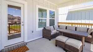 A covered porch with wicker furniture, a door with a view of a house, and a wooden bench. - Bring The Whole Family And Friends, Too! White Beaches Are Waiting! (Perdido Key)