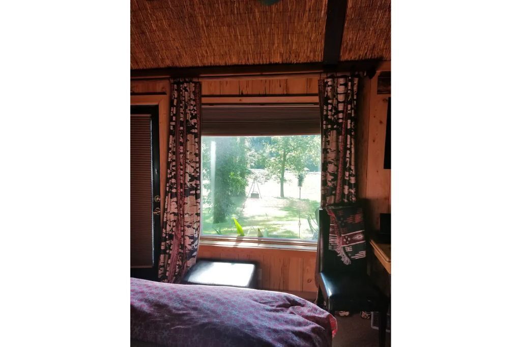 Una habitación con cama, ventana con cortinas, escritorio y silla.