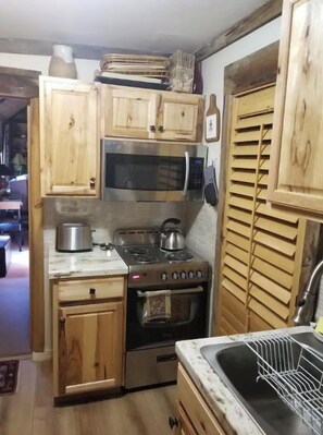 A compact kitchen with wooden cabinets, a stainless steel stove, a microwave, and a sink. - Cottage on riverbank one mile from Clarksdale in gated community (Clarksdale)