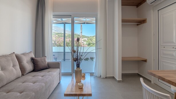 A modern living room with a sofa, a wooden coffee table, and a view of a mountainous landscape through large windows. - Secretnest 17 apartment near the beach, Plakias (Plakias)