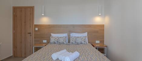 A neatly made bed with a striped bedspread and two pillows, a wooden door, and bedside tables with lamps.