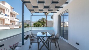 A balcony with a table and chairs, a glass railing, and a view of buildings and trees. - Secretnest 17 apartment near the beach, Plakias (Plakias)