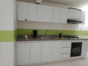 Cocina compacta con armarios blancos, una franja verde, un lavamanos, una estufa y un lavavajillas.