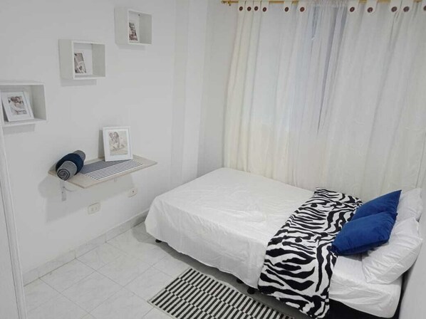 Un dormitorio con una cama, un estante con una toalla enrollada y un pequeño marco en la pared.