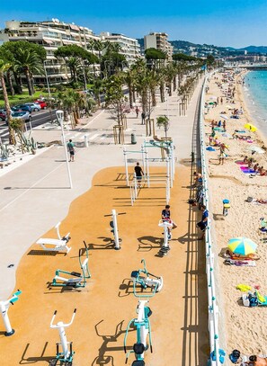 A beach with exercise equipment, a promenade, and buildings in the background. - NEW HOUSE IN CANNES, with access to the pool, a 4-minute walk from the beach, RIGHT ON THE BEACH (Cannes)