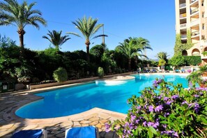 A swimming pool with lounge chairs, palm trees, and a building with balconies.