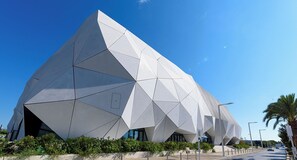 A modern architectural building with a geometric design, featuring a prominent triangular facade and a series of windows.