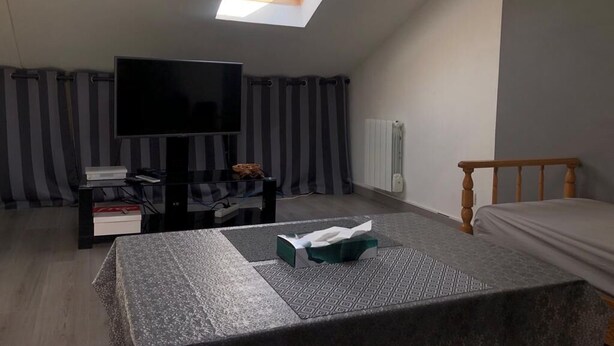 Une chambre avec une lucarne, un lit, une télévision et une table de chevet avec des livres et une boîte de mouchoirs.