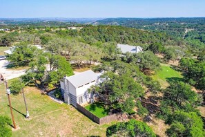 Une grande maison de plain-pied, à l’extérieur blanc et dotée d’un toit plat, entourée d’une végétation luxuriante et d’arbres.