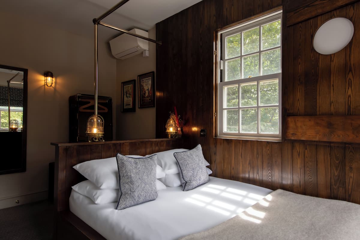 Ein Schlafzimmer mit einem hölzernen Kopfteil, einem großen Fenster und einem Nachttisch mit einer Lampe.
