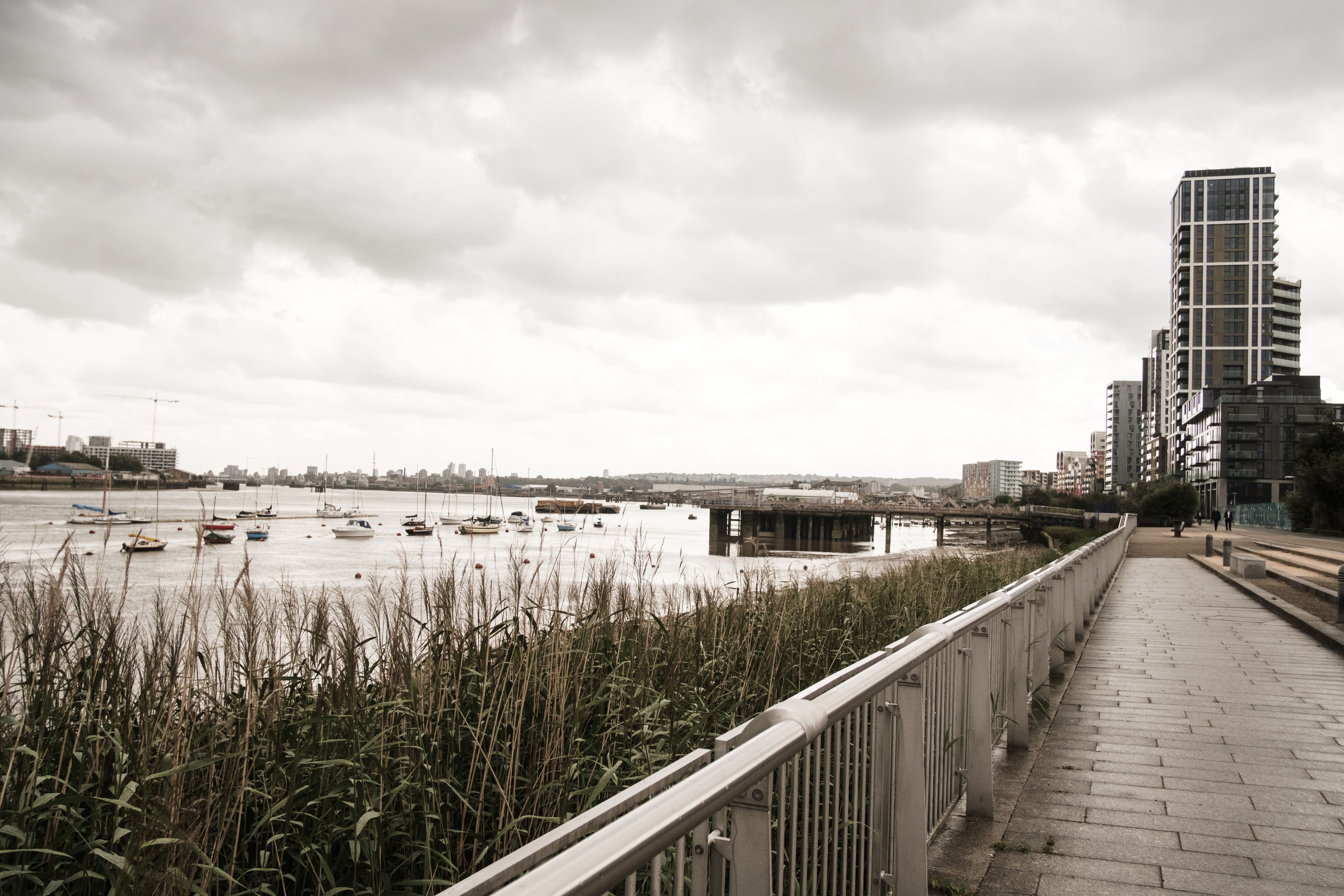 A riverside walkway with a modern building on the right and boats on the water.