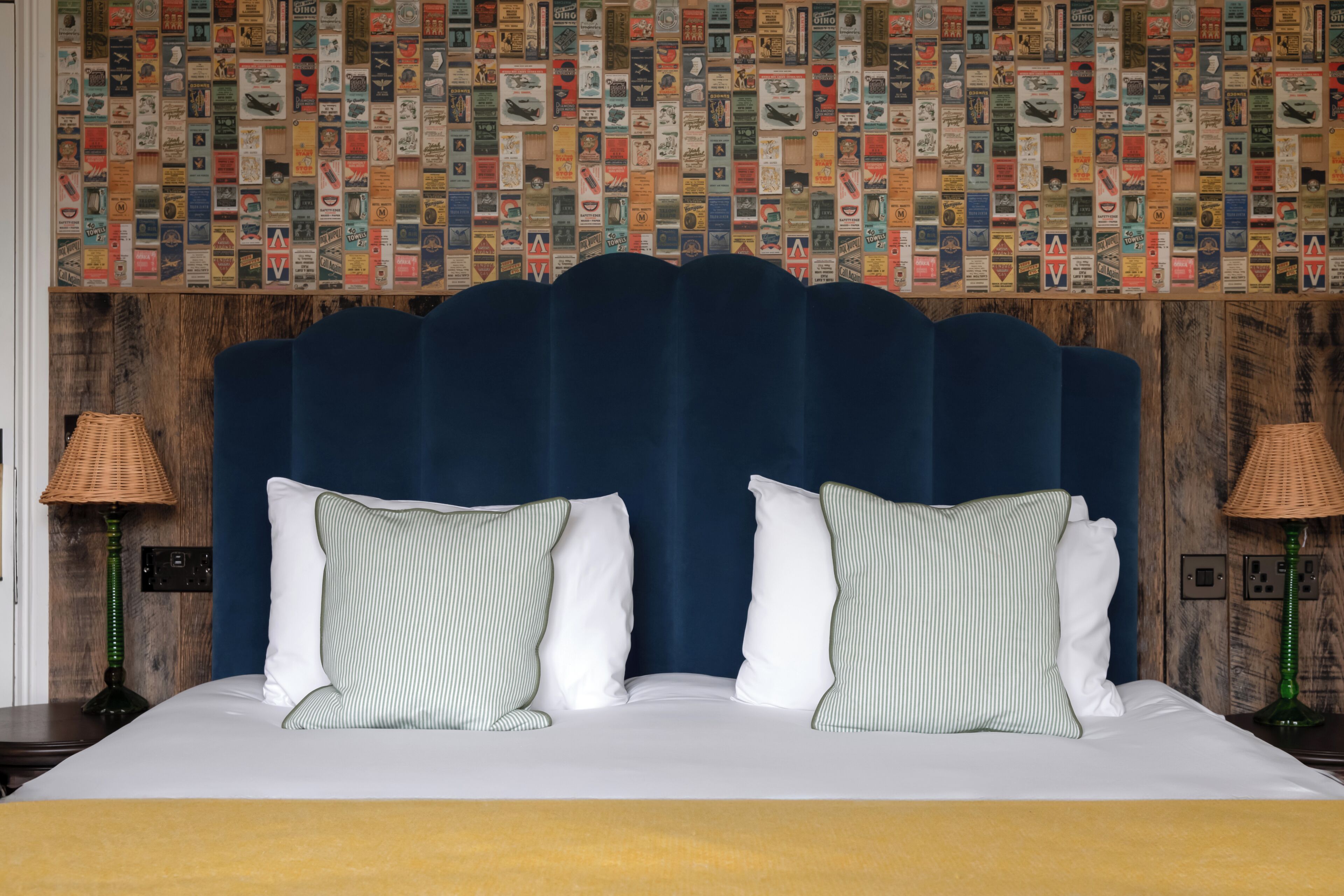 A hotel room with a large bed, striped pillows, and a wall covered with postcards.