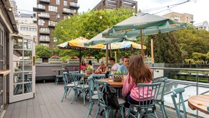 An outdoor patio with tables and chairs, umbrellas, and potted plants. - The Pilot (London)