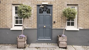 A building with a dark grey door, two windows on either side, and a brick facade. - The Pilot (London)