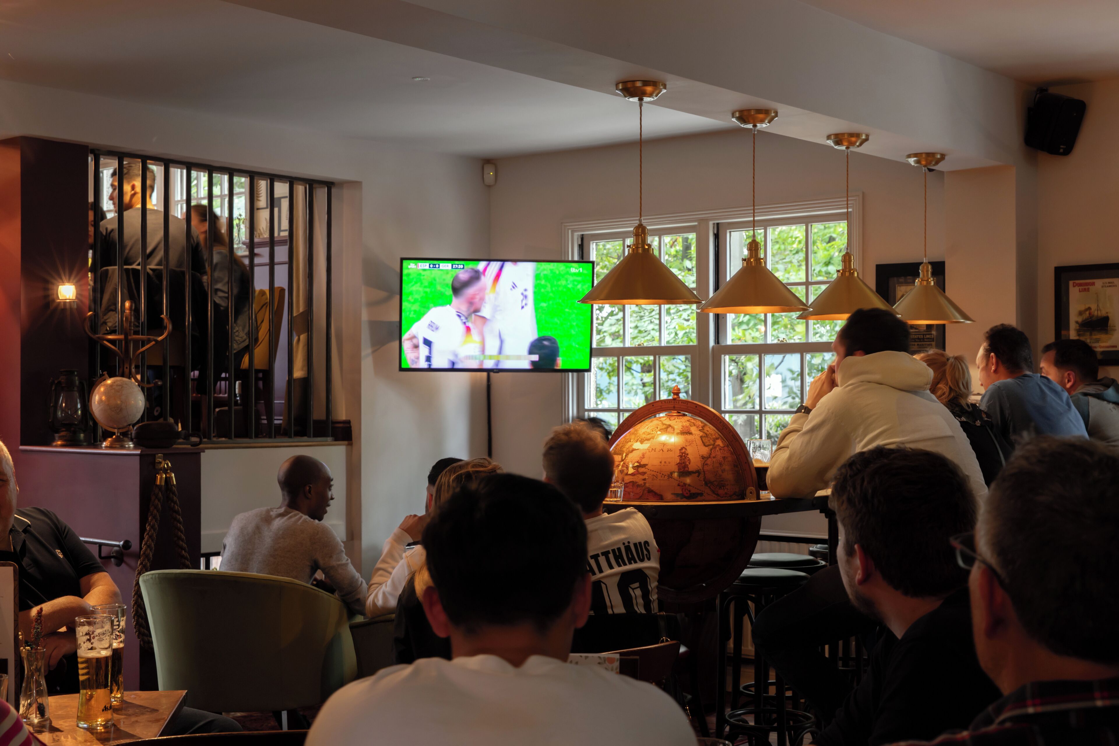 Un bar où des clients regardent un écran de télévision, avec un globe terrestre et des lampes suspendues.