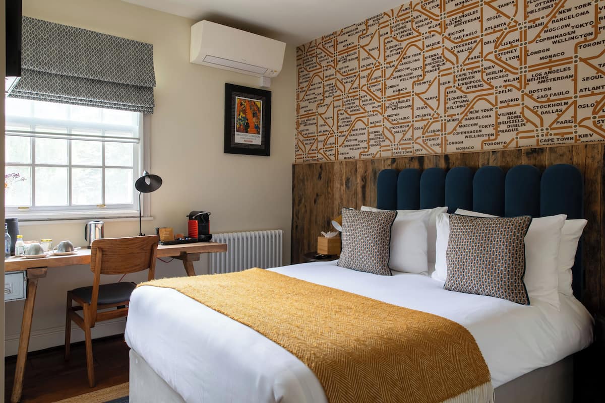 Ein Hotelzimmer mit einem großen Bett, einem Holztisch, einem Stuhl, einer Heizung und einer Wand mit Städtenamen.