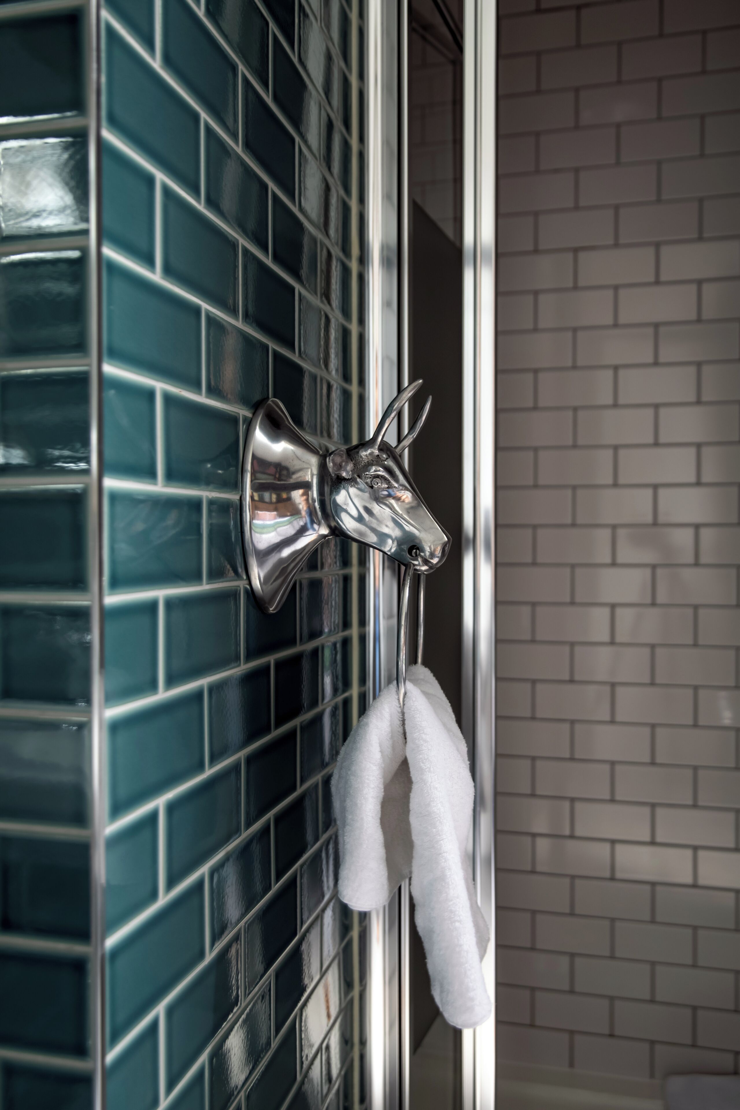 A bathroom with a blue-tiled wall, a chrome towel rack, and a white towel hanging on it.