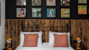 A bedroom with a bed, two nightstands, a wooden headboard, and a wall decorated with framed posters. - The Pilot (London)