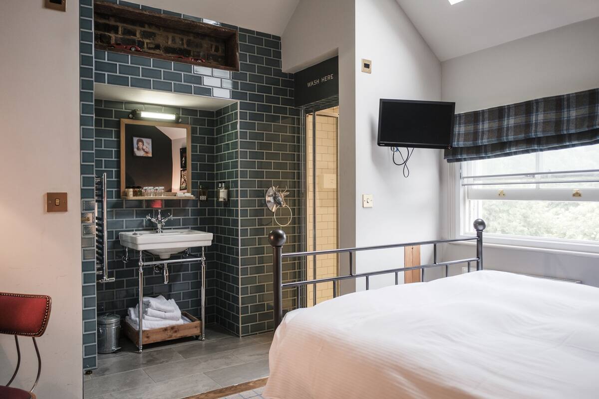 Ein Schlafzimmer mit Bett, ein Badezimmer mit Waschbecken und Spiegel sowie ein an der Wand befestigter Fernseher.