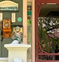 Una puerta con una estatua decorativa de ángel, un teléfono antiguo y un letrero de bienvenida con un paisaje urbano.