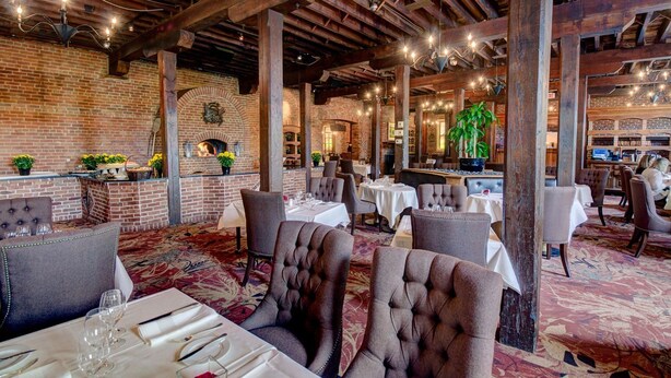 A restaurant with brick walls, wooden beams, and a variety of seating arrangements including booths and tables. - WeatherPine Inn (Niagara-on-the-Lake)
