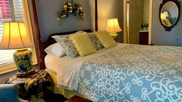 A neatly made bed with patterned bedding, a bedside table with a lamp, a chair, and a mirror on the wall.