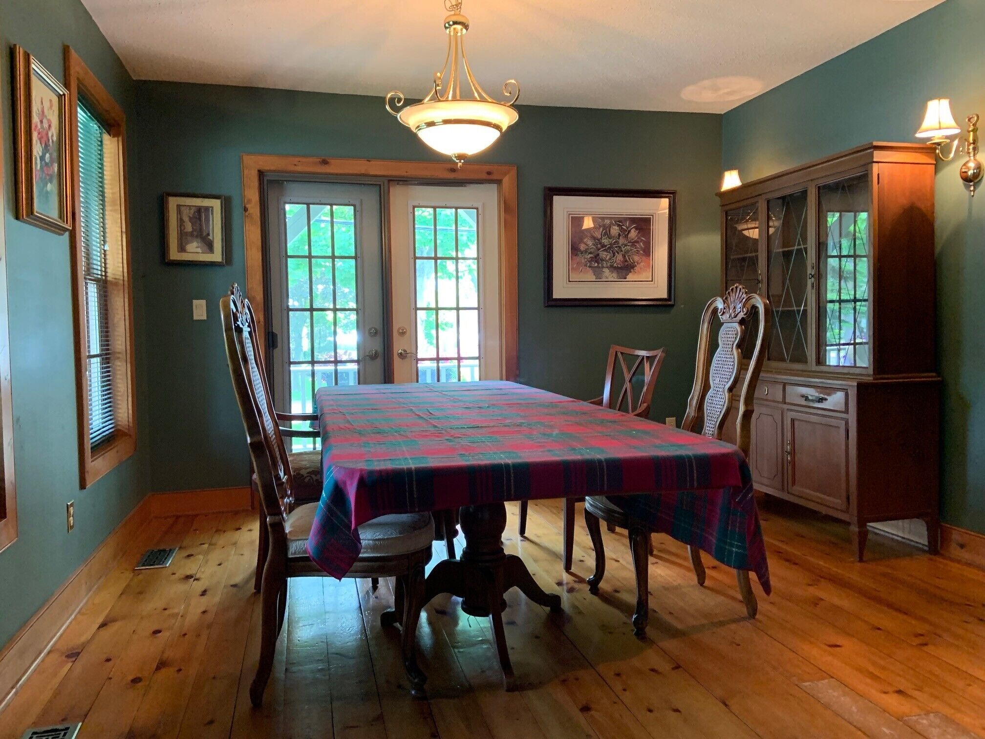 A dining room with a wooden table, chairs, and a chandelier. There are framed pictures on the walls and a cabinet with glass doors.