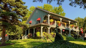 A large, two-story house with a porch, surrounded by lush greenery and trees. - WeatherPine Inn (Niagara-on-the-Lake)