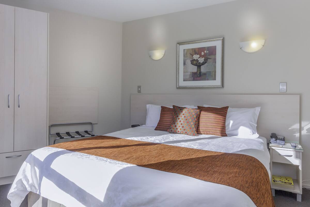 Hotelkamer met een groot bed, een kledingkast, nachtkastje met lamp en een lijst aan de muur.