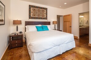 A neatly arranged bedroom with a large bed, two bedside tables, a wooden headboard, and a patterned wall hanging.